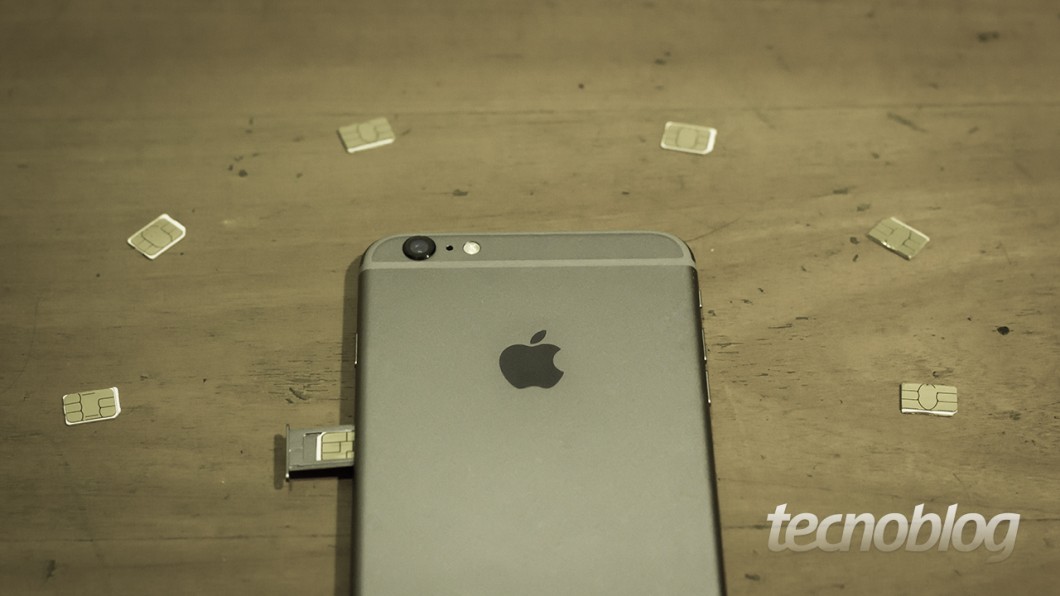 Foto de um iPhone sobre mesa de madeira, rodeado por vários cartões SIM