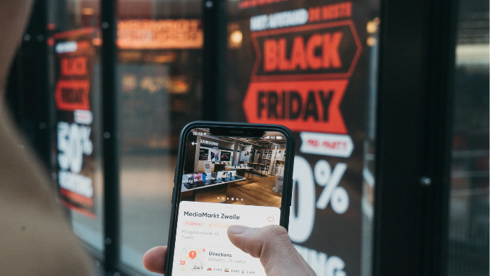 pessoa com celular na mão em frente a uma loja com a placa de black friday