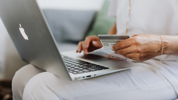 pessoa com notebook no colo segurando um cartão de crédito