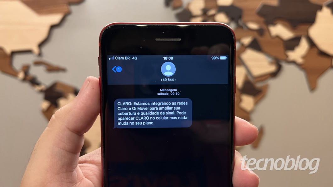 Celular mostrando mensagem SMS: "Estamos integrando as redes Claro e Oi Movel para ampliar sua cobertura e qualidade de sinal. Pode aparecer CLARO no celular mas nada muda no seu plano."