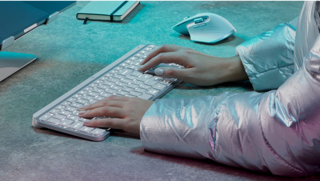 Teclado branco Logitech MX Keys S sendo usado por pessoa de blusa prateada, com braços e mãos aparentes na imagem