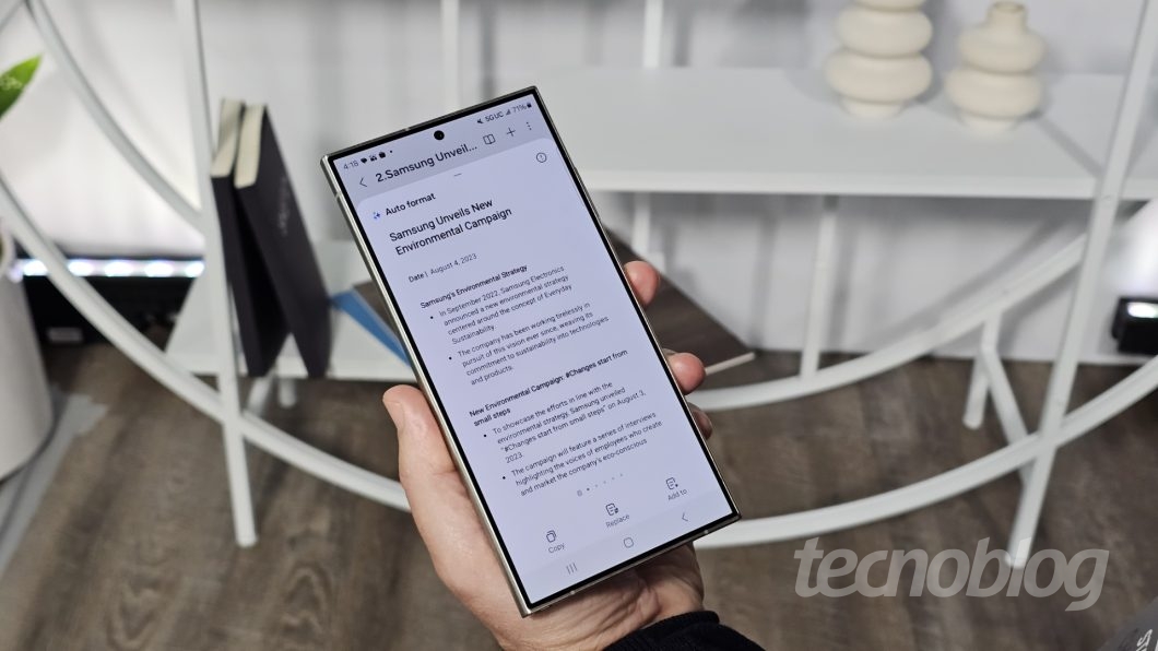 Mão segurando smartphone, exibindo texto na tela do aparelho
