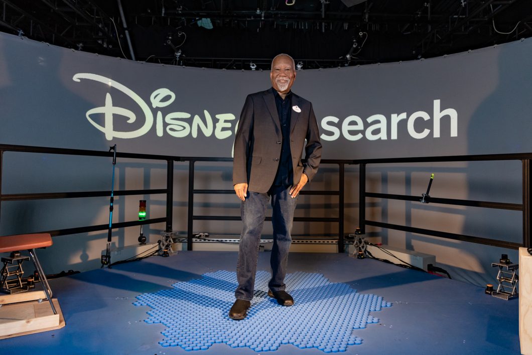 Homem idoso em cima do piso móvel HoloTile com o logo da Disney Research ao fundo