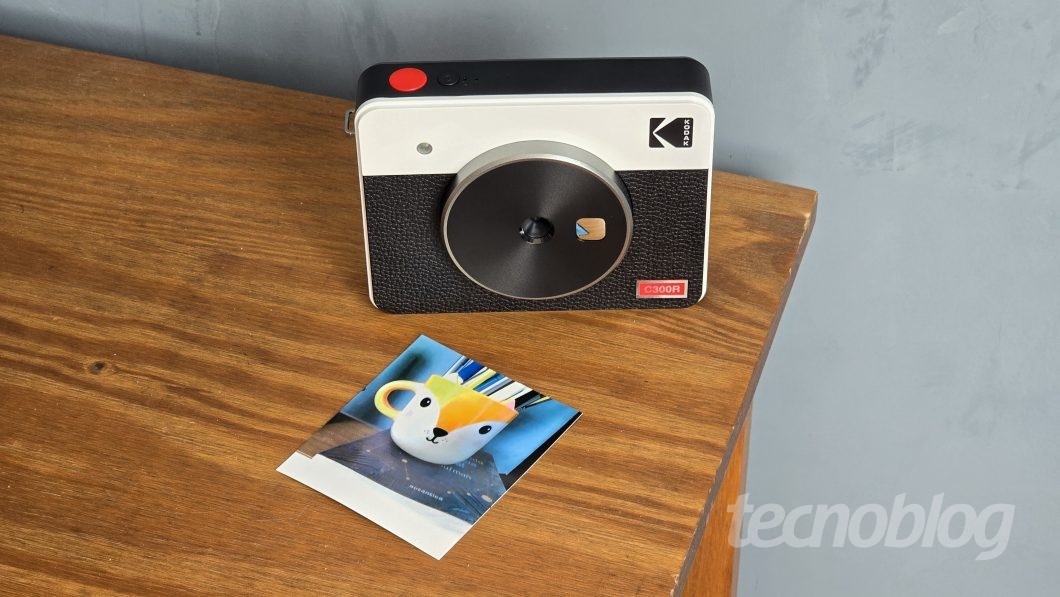 Câmera instantânea da Kodak sobre mesa de madeira, junto de uma foto impressa