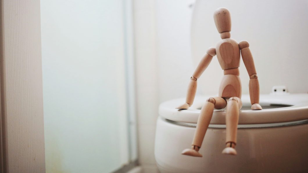 Boneco de madeira sentado na borda de um vaso sanitário