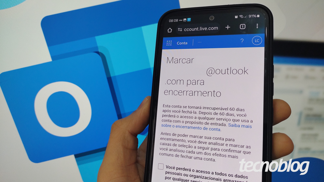 Uma mão segura um celular Samsung que exibe a tela de exclusão de um e-mail Outlook. Ao fundo, uma imagem exibe o logo do Outlook