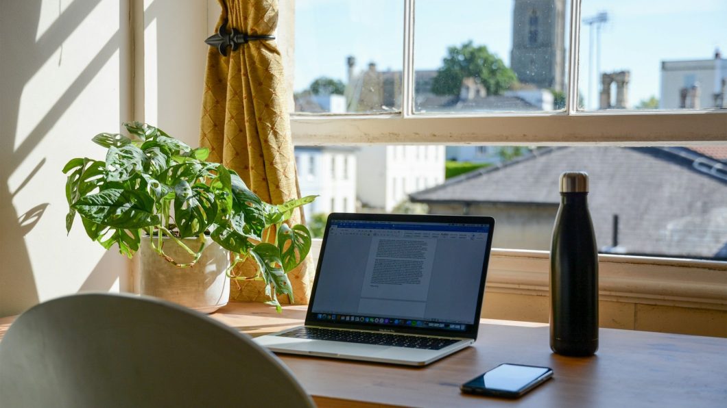 Escrivaninha em casa, com notebook, mouse, plantinha e garrafa