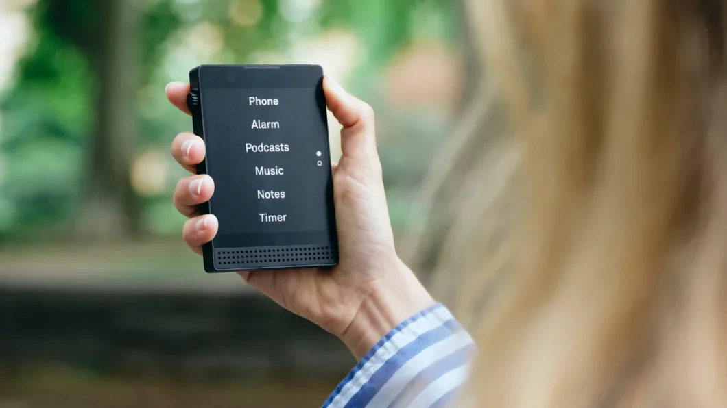 Pessoa de cabelo loiro segura um Light Phone 3, smartphone pequeno com tela em preto e branco e interface de texto