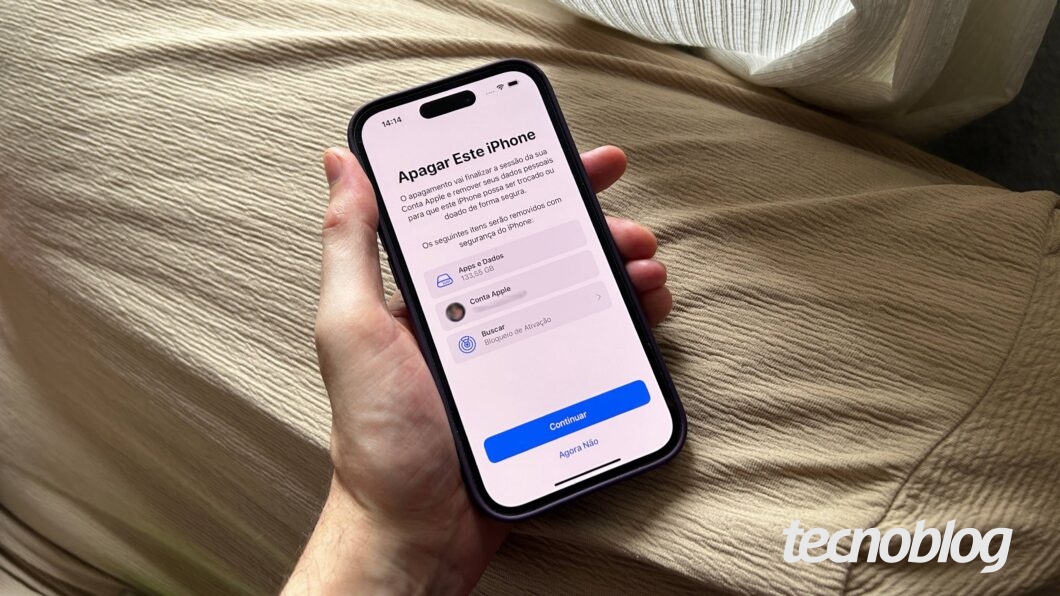 Uma mão segura um iPhone exibindo a tela "Apagar Este iPhone"