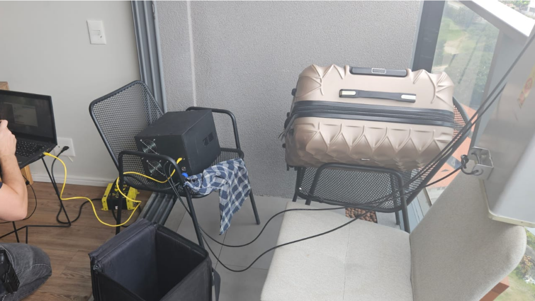 Fotografia de um equipamento de telecomunicações posicionado em sala de apartamento. À direita há uma grande antena, posicionada na varanda.