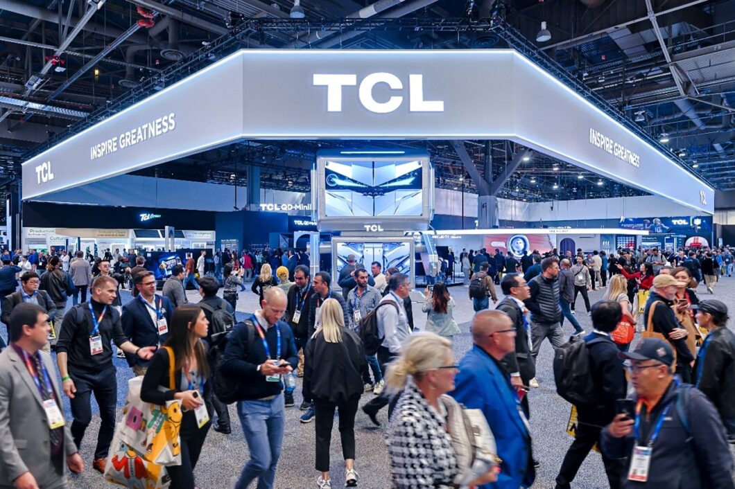 Estande da TCL na CES. Há uma estrutura suspensa com o logo da TCL e a frase Inspire Greatness. Várias pessoas passam diante do estande.