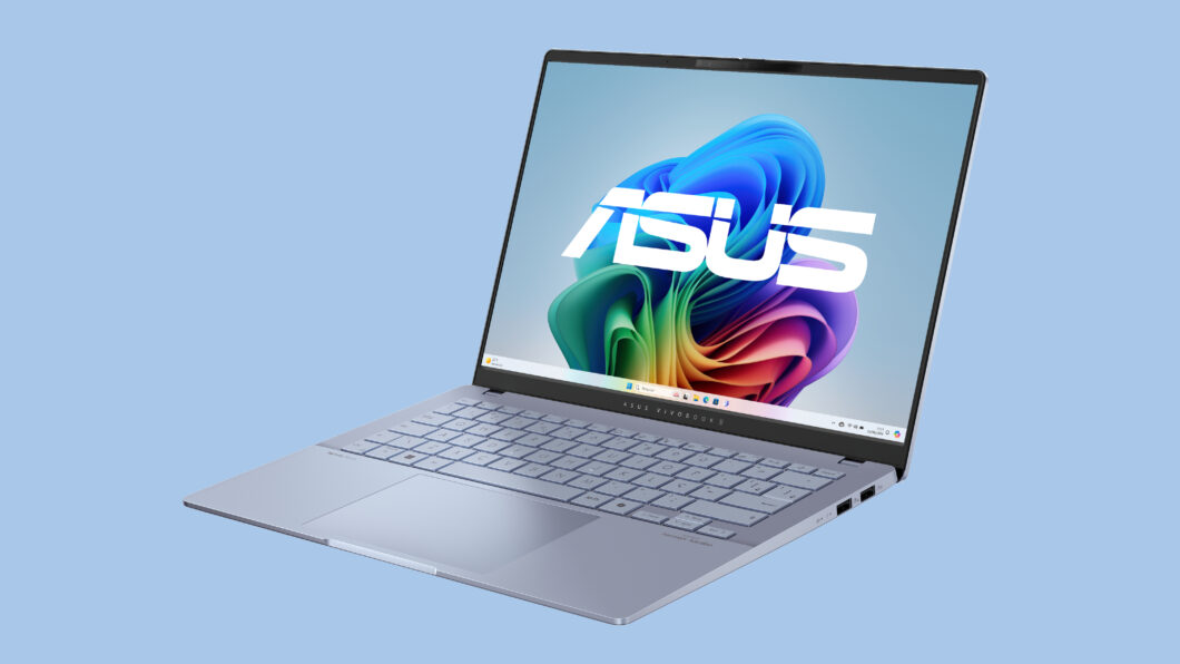 Fotografia colorida mostra um Asus Vivobook S 14 prateado aberto em um fundo de cor azul.