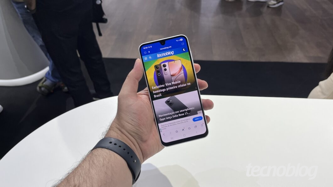 Foto de smartphone na mão com o site do Tecnoblog aberto