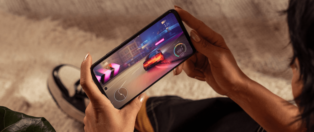 Imagem mostra celular Moto G35 nas mãos de uma mulher. Na tela, há a exibição de um jogo de corrida com cores vibrantes, em tons de vermelho, azul e roxo.