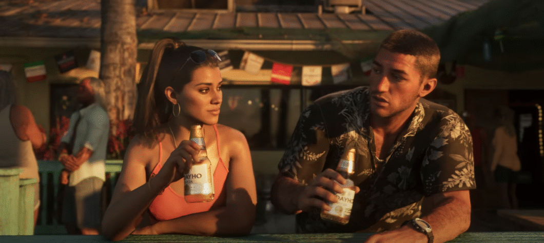 Imagem mostra um homem e uma mulher estão sentados lado a lado, segurando garrafas de cerveja, ambos personagens do jogo GTA 6. A mulher, à esquerda, tem cabelos castanhos presos em um rabo de cavalo, usa óculos de sol na cabeça e uma blusa laranja. Ela olha para a esquerda. O homem, à direita, tem cabelo curto e castanho e veste uma camisa estampada florida. 