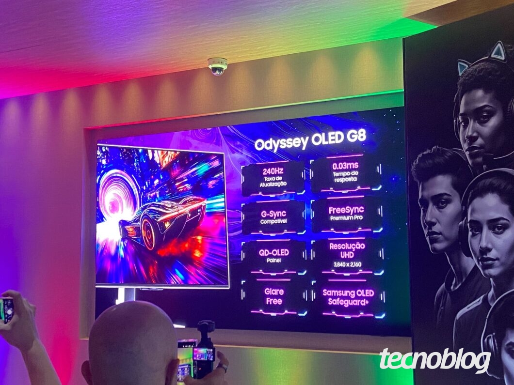 Imagem mostra uma TV de tela grande exibindo informações sobre o "Odyssey OLED G8". No lado esquerdo da tela, a imagem vibrante de um carro em neon. No lado direito, uma lista de recursos em texto branco sobre fundo azul escuro, incluindo "240Hz Taxa de Atualização", "0.03ms Tempo de resposta" e "Resolução UHD 3.840 x 2.160". O logotipo "tecnoblog" está no canto inferior direito.