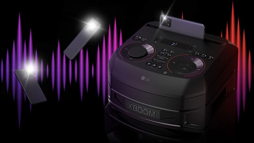 Imagem mostra uma caixa de som preta LG XBOOM RNC9 ao centro, com um smartphone posicionado verticalmente em um slot na parte superior. Ondas sonoras vibrantes em tons de roxo e vermelho emanam dos lados da caixa de som contra um fundo preto. A marca "LG" é visível na frente da caixa de som, e a palavra "XBOOM" está inscrita em letras grandes na parte inferior.