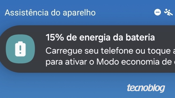 Notificação na tela de um smartphone com fundo azul e título "Assistência do aparelho". Mensagem exibida em destaque informa: "15% de energia da bateria. Carregue seu telefone ou toque aqui para ativar o Modo economia de energia". Ao lado esquerdo, ícone de uma bateria com nível baixo.