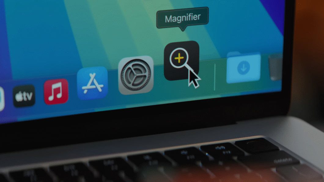 Close-up da tela de um Mac exibindo o Dock do macOS com o cursor do mouse posicionado sobre o ícone do novo aplicativo Lupa (Magnifier)
