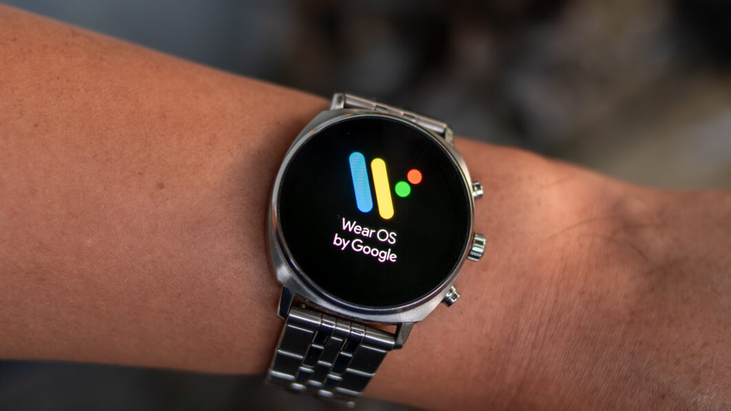 Pessoa vestindo um smartwatch. A tela está ligada com o símbolo do sistema operacional Wear OS.