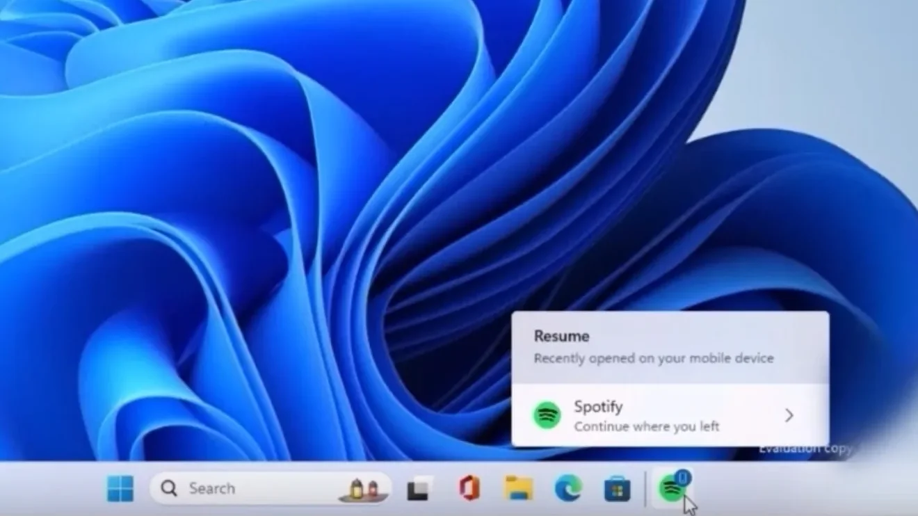 Captura de tela do Windows 11 com foco no ícone do Spotify na barra de tarefas. Ao clicar no ícone, aparece um popup com as mensagens: "Resume - Recently opened on your mobile device" e "Spotify - Continue where you left", indicando a retomada da reprodução de música iniciada em outro dispositivo.