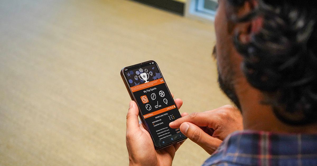 Foto de smartphone na mão de homem usando um aplicativo de apostas (bets)