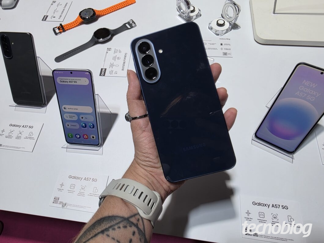 Galaxy A57 5G sendo mostrado em mãos, com tela e traseira exibidas e acessórios/embalagens ao redor