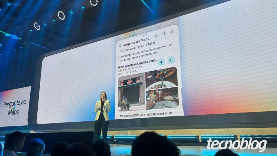 Executiva no palco. Atrás, um telão mostrando interface conversacional do Pergunte ao Maps.
