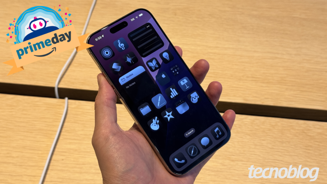 Pessoa segurando um iPhone com ícones de aplicativos na tela, com o selo “primeday” e marca “tecnoblog”