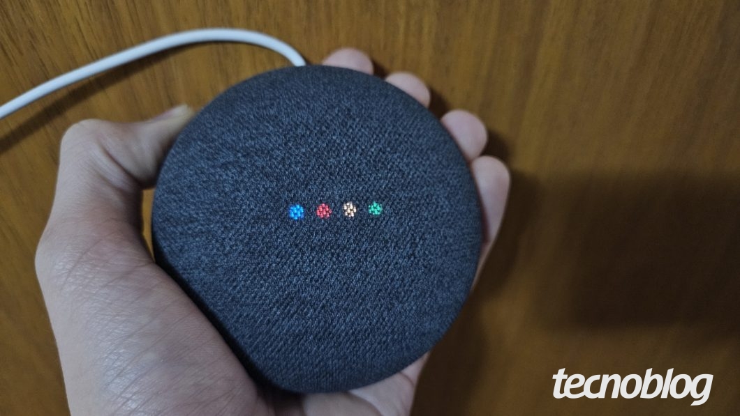 Mão segurando alto falante inteligente Google Nest Mini com 4 LEDs coloridos acesos nas cores do  Google