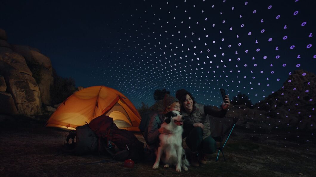 Imagem mostra um acampamento à noite com pessoas usando smartphone sob padrão de conexão por satélite