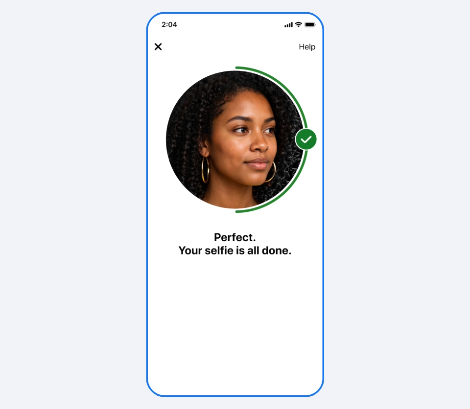 Captura de tela de smartphone exibindo uma interface com fundo branco. No centro, uma imagem circular exibe o rosto de uma mulher negra de cabelos cacheados e brincos de argola. O círculo é contornado por uma linha verde com um ícone de verificação. Abaixo da foto, o texto em negrito diz: "Perfect. Your selfie is all done.".