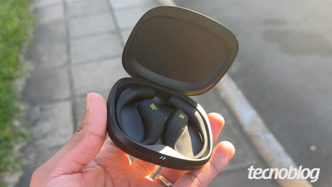 Mão segurando a case aberta do JBL Endurance Zone, com os fones open ear abrigados no interior