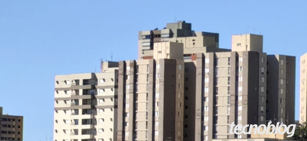 Foto tirada em 5x pela câmera principal de 50 MP, mostrando prédios em zoom no céu azul