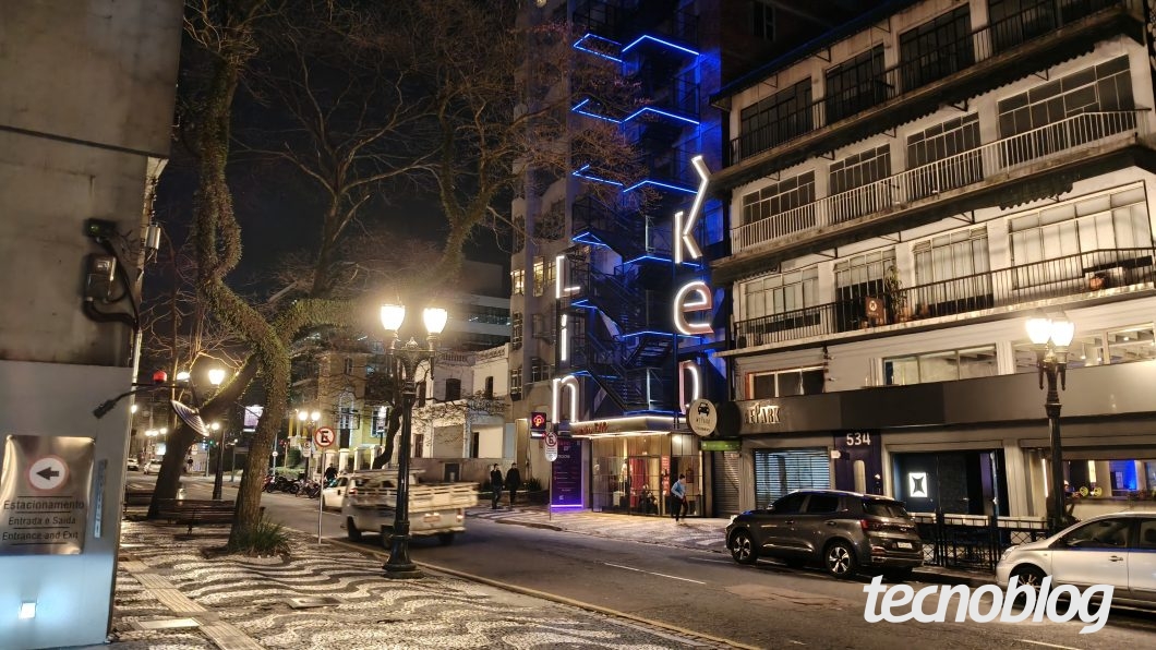 Foto tirada com a câmera principal de 50 MP à noite, mostrando rua iluminada e fachadas com luzes neon