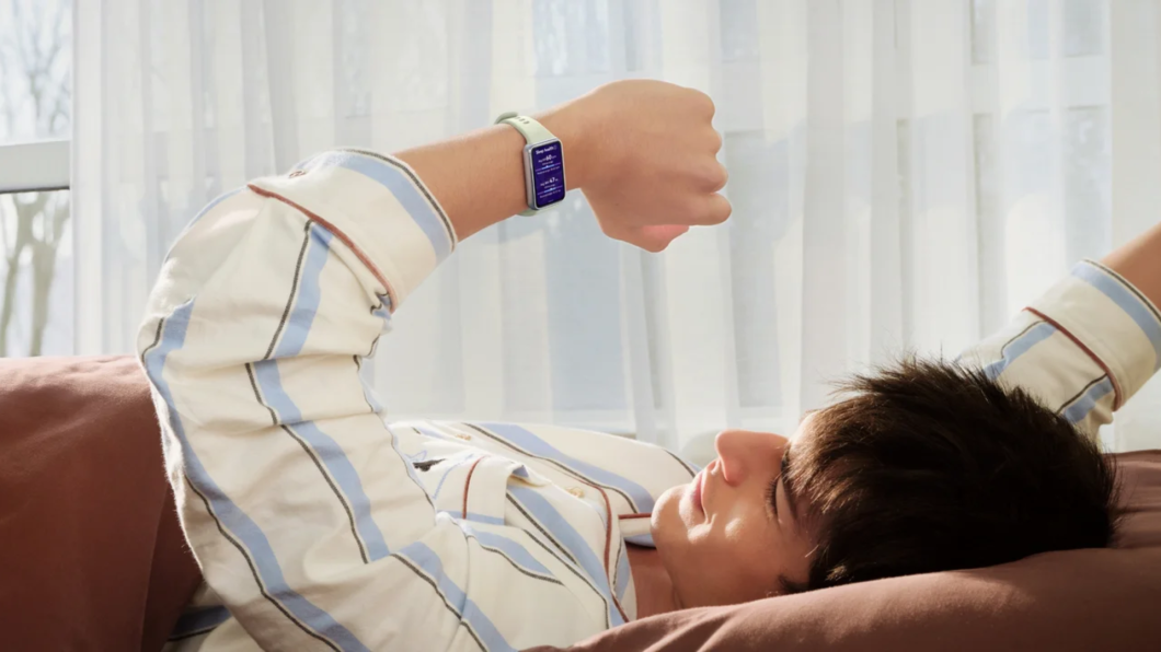 Homem deitado espreguiçando-se em uma cama e olhando para a tela da Huawei Band 11 no seu pulso esquerdo