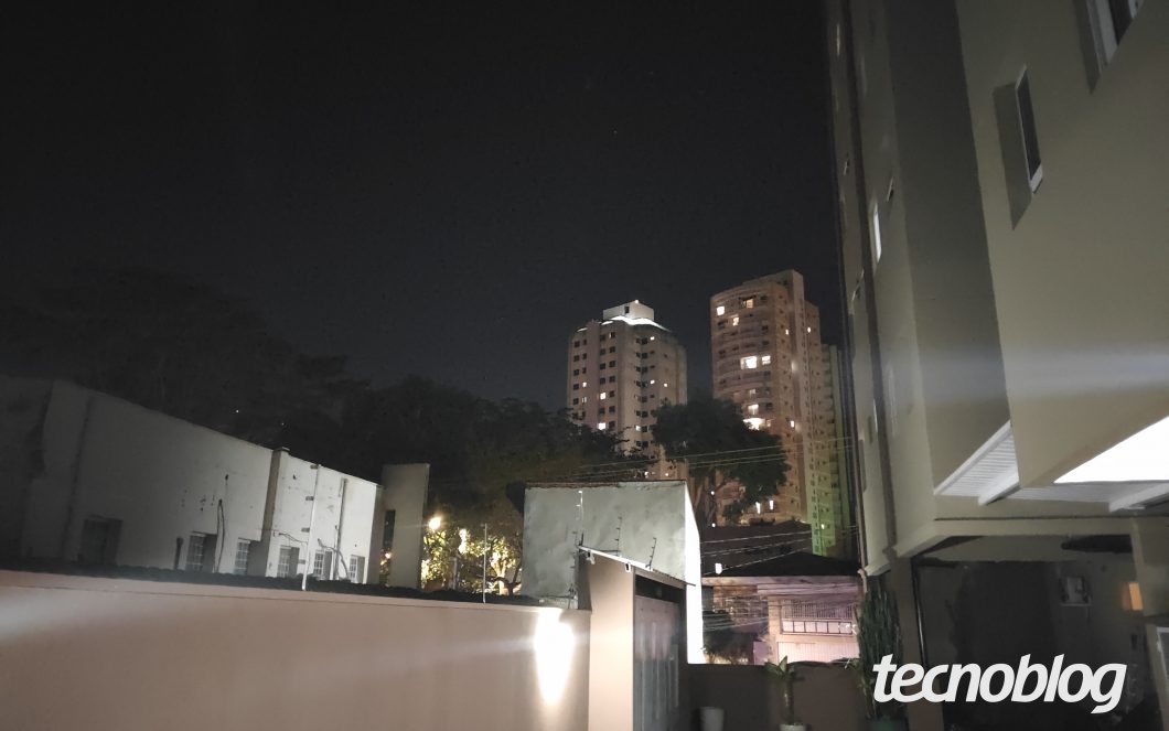Prédio e torres iluminadas vistos à noite a partir do pátio, com céu escuro ao fundo