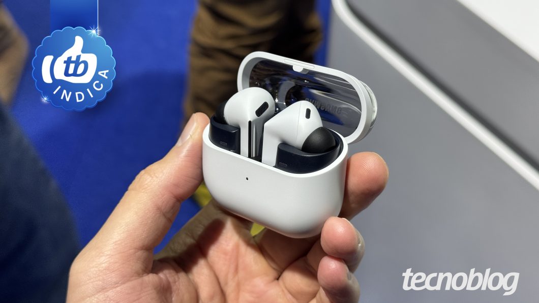 Fones sem fio brancos em estojo aberto, sendo segurados na mão, com marca TecnoBlog ao fundo