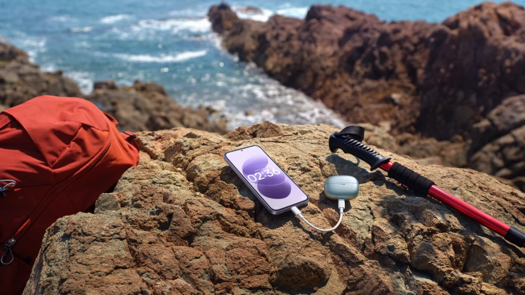 Carregamento reverso: smartphone sendo alimentado por um power bank externo em um cenário ao ar livre, na praia